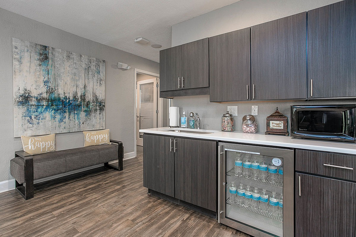 Modern kitchen in Autumn Ridge's Clubhouse with sleek dark wood cabinets, contemporary artwork, and elegant seating area on wood flooring.