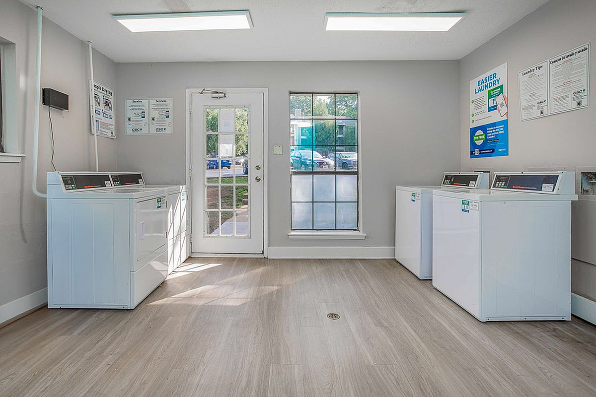 Bright communal laundry room with modern washing machines, natural light pouring through large windows, and sleek wooden flooring at Autumn Ridge Apartments.