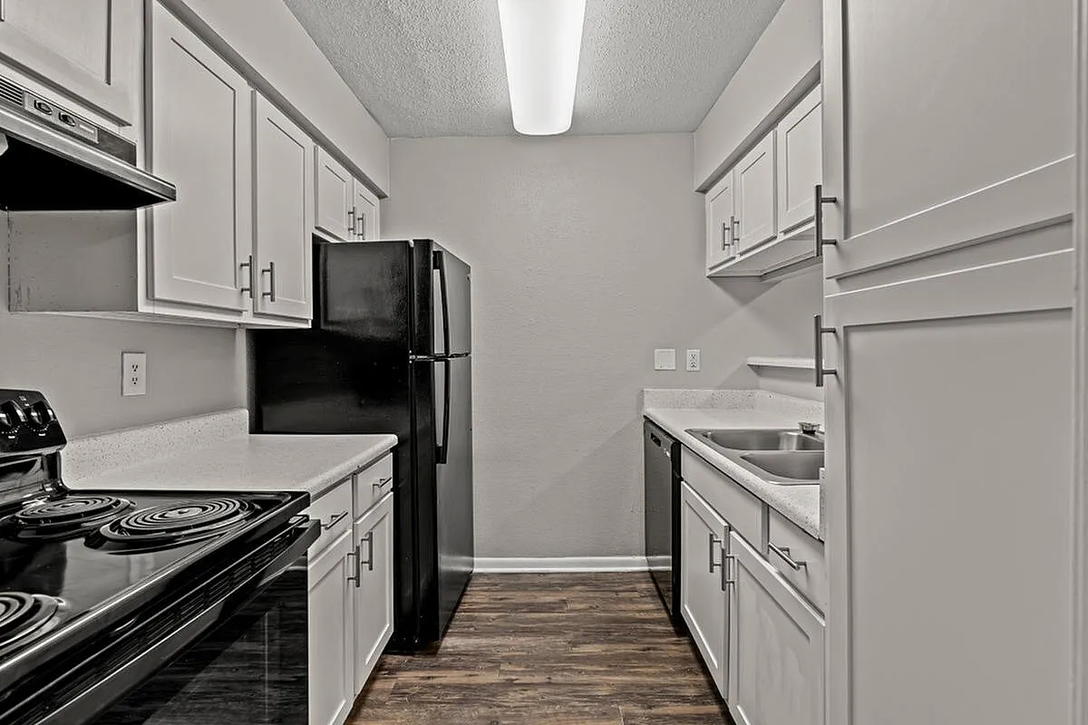 Contemporary kitchen with sleek black appliances, elegant white cabinetry, and a polished wood floor at Autumn Ridge Apartments.