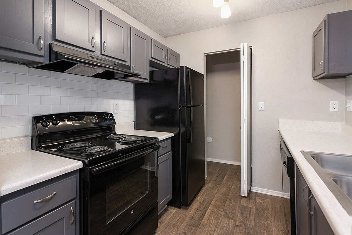 Modern kitchen at Park at Oak Ridge Apartments with sleek gray cabinetry, elegant black appliances, and chic wood flooring.