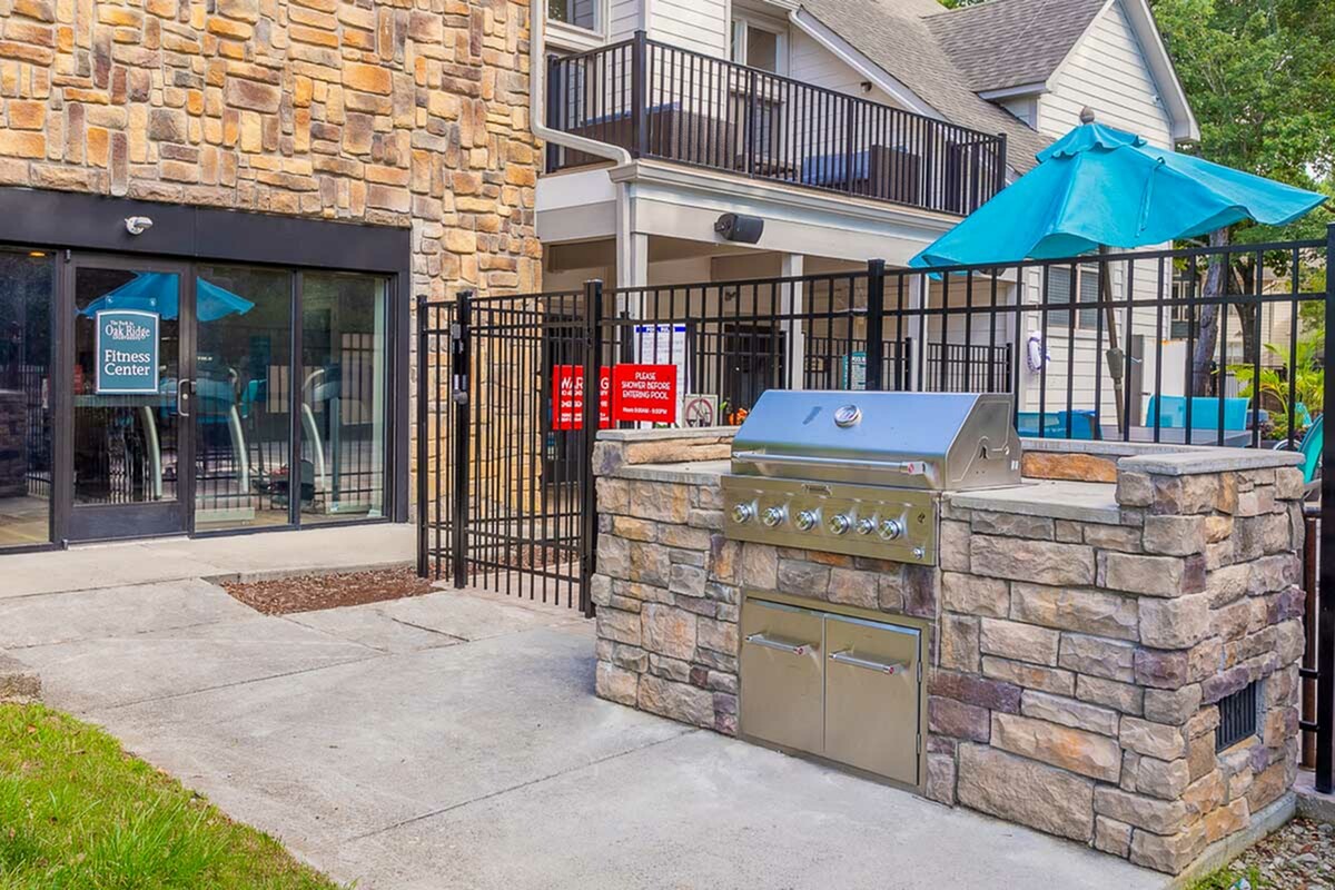 Inviting outdoor area featuring a modern stone barbecue grill beside a welcoming fitness center entrance, perfect for relaxation and community gatherings at Park at Oak Ridge.