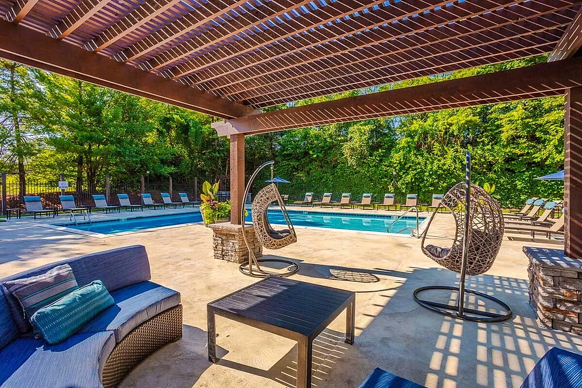Luxurious outdoor pool area at Timber Hollow Apartments with cozy seating, stylish hanging chairs, and lush greenery, perfect for relaxation and entertaining.