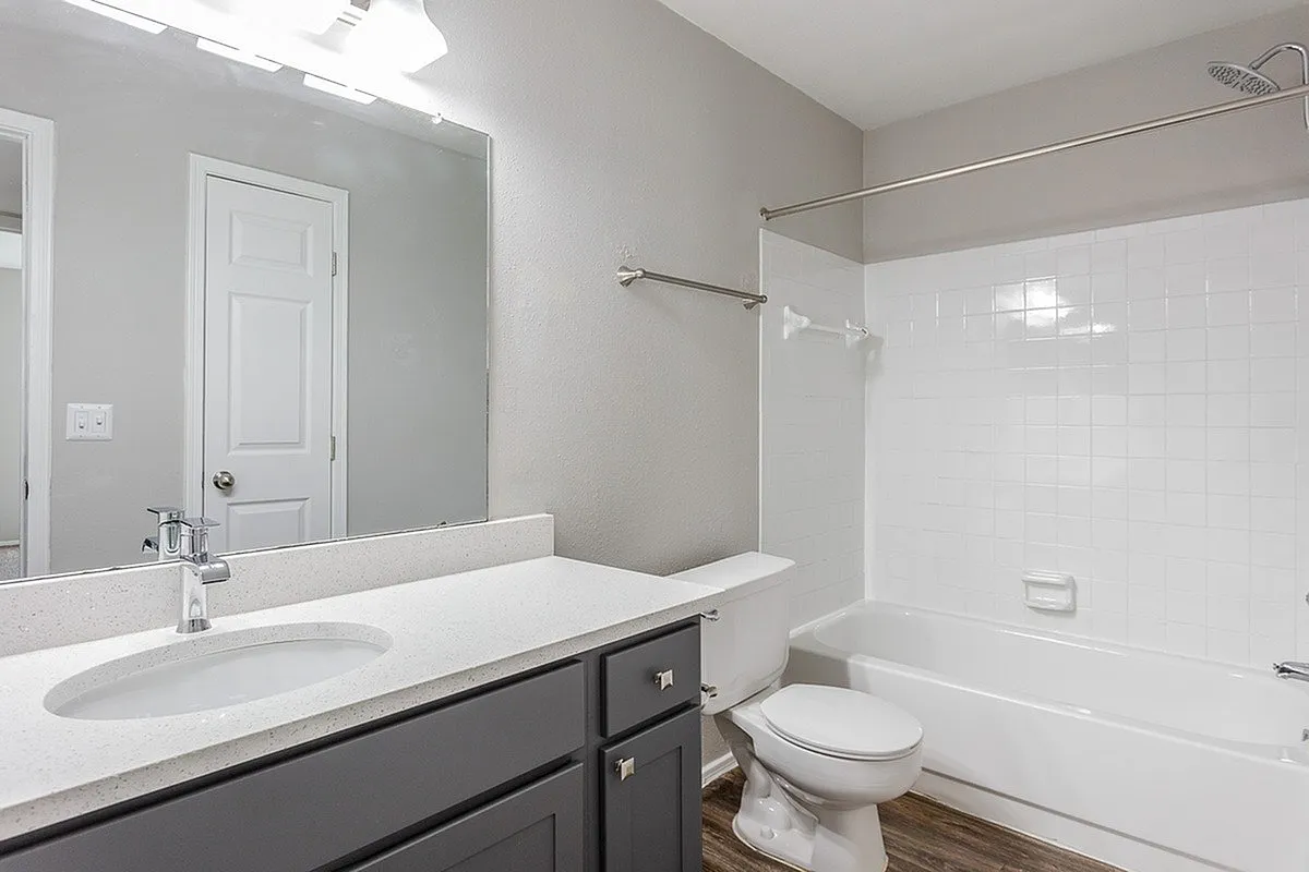 Modern bathroom at Timber Hollow Apartments with elegant white countertops, sleek fixtures, and a pristine bathtub for a relaxing retreat.