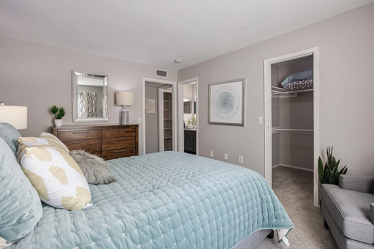 Inviting bedroom in modern apartment featuring a plush bed with stylish bedding, elegant wooden dresser, and a cozy walk-in closet at Timber Hollow Apartments.