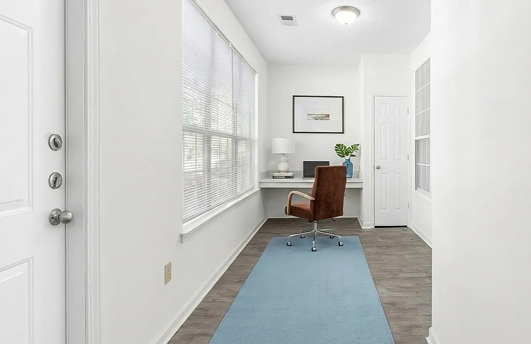 Bright and inviting home office space with large windows, elegant brown chair, and sleek desk. Perfectly designed for productivity  at Lake St James Apartments in Conyers GA