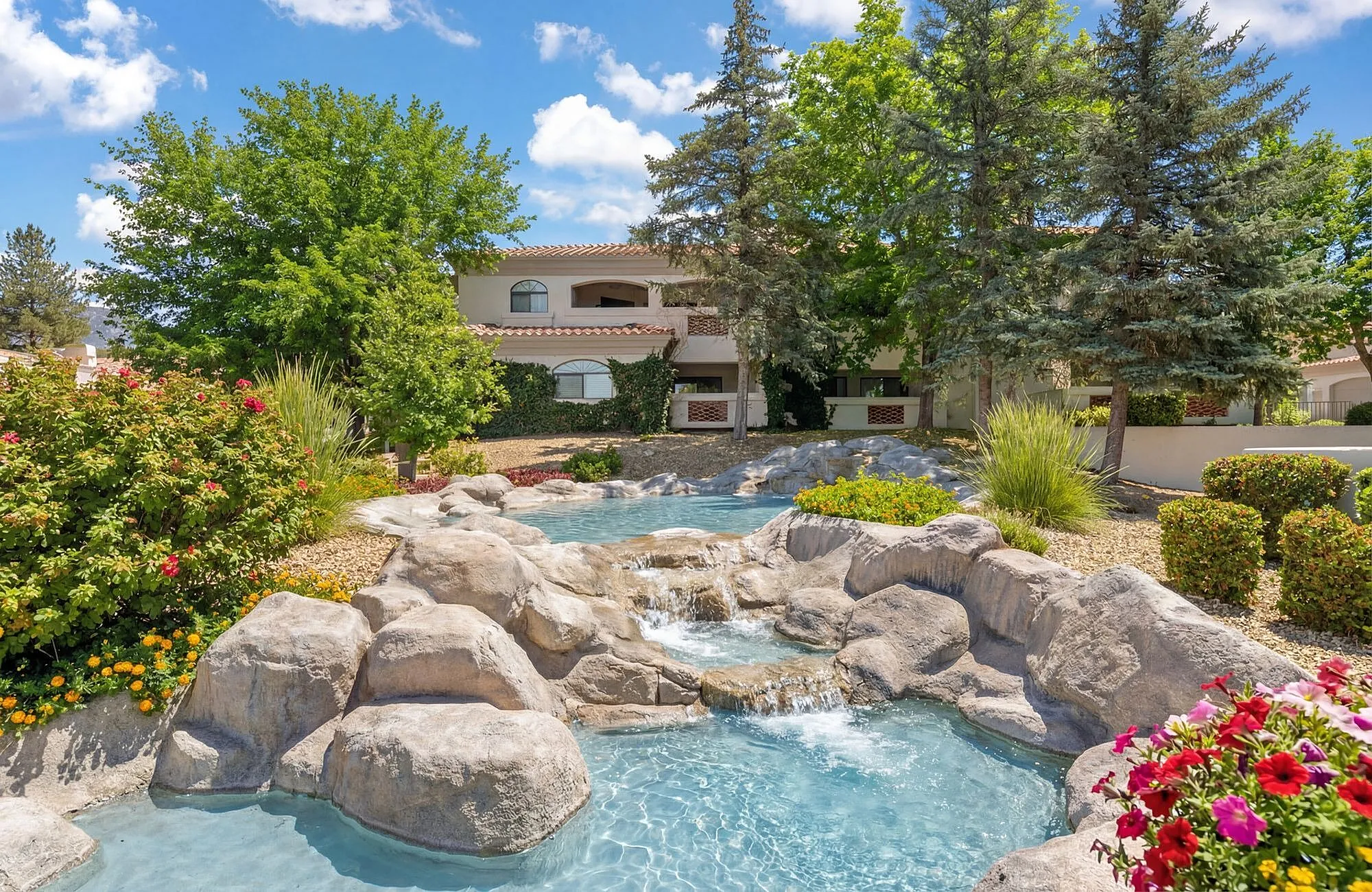 Charming apartment complex with a picturesque rock waterfall feature surrounded by vibrant flowers and lush greenery at Pavilions Apartments in Albuquerque.