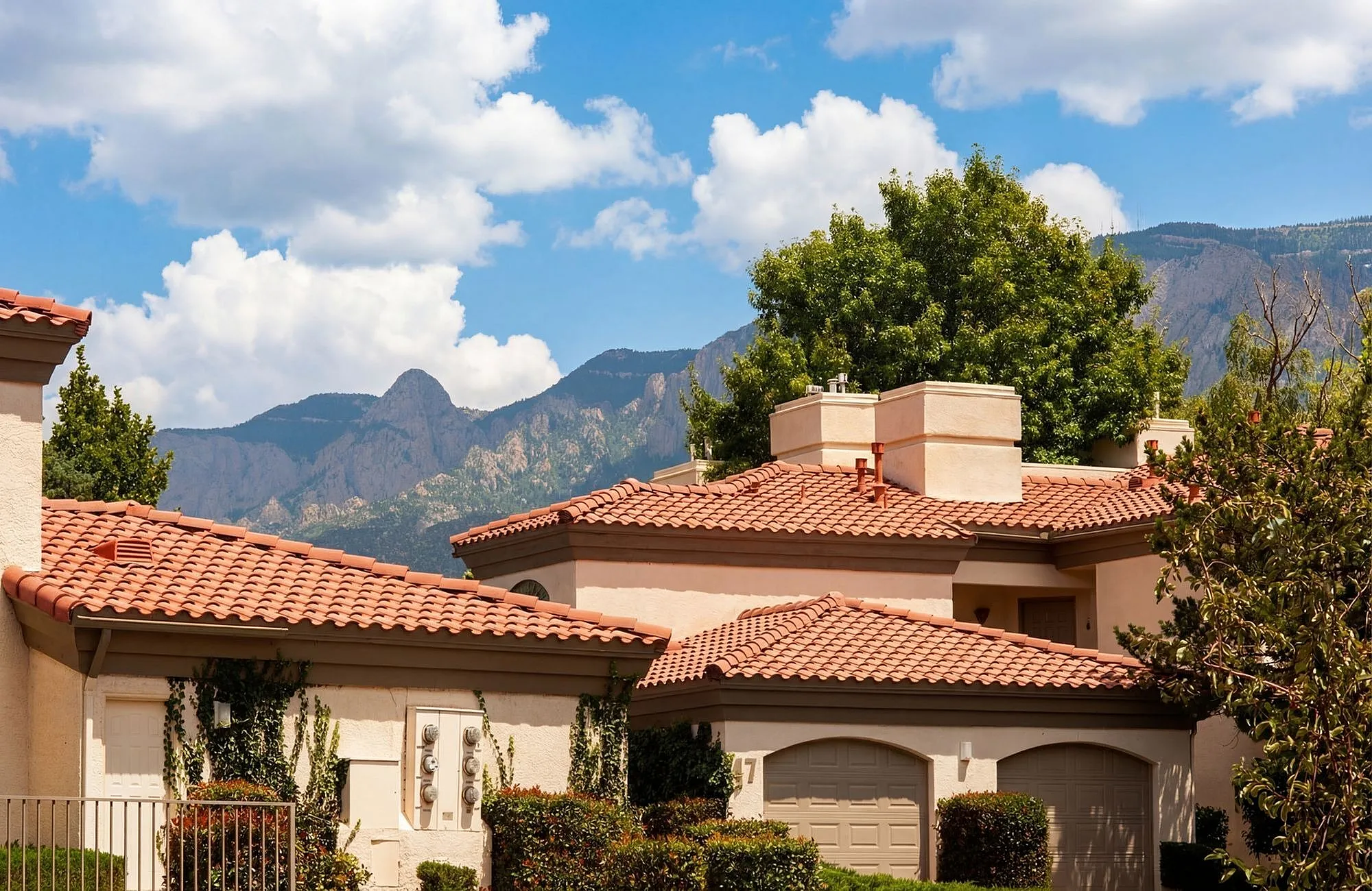 Charming homes with terracotta roofs set against a stunning mountain backdrop, surrounded by lush greenery and blue skies at Pavilions Apartments in Albuquerque.