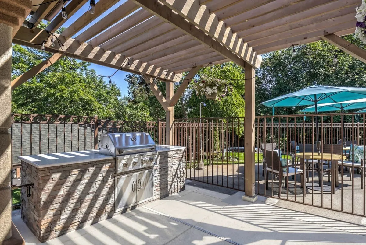 Charming outdoor patio with rustic pergola, stylish BBQ area, and inviting seating under vibrant umbrellas.