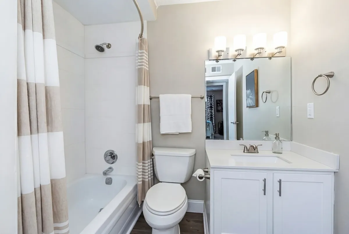 Elegant bathroom with a modern design featuring a clean white vanity, framed mirror, and a soothing shower-tub combo with a stylish striped curtain.