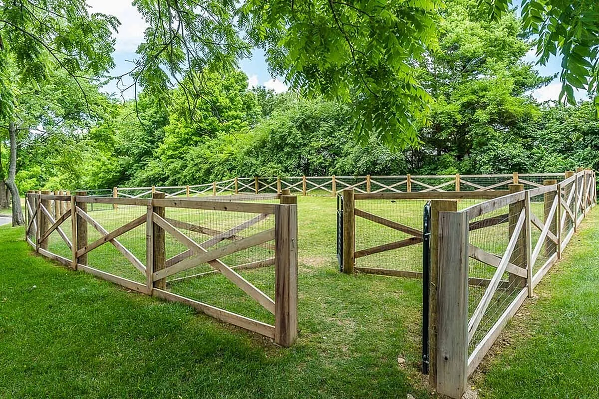 Charming outdoor dog park space with a wooden fence, lush greenery, and a serene, natural setting perfect for relaxation or pet activities at The Colony at the Oaks Apartments.