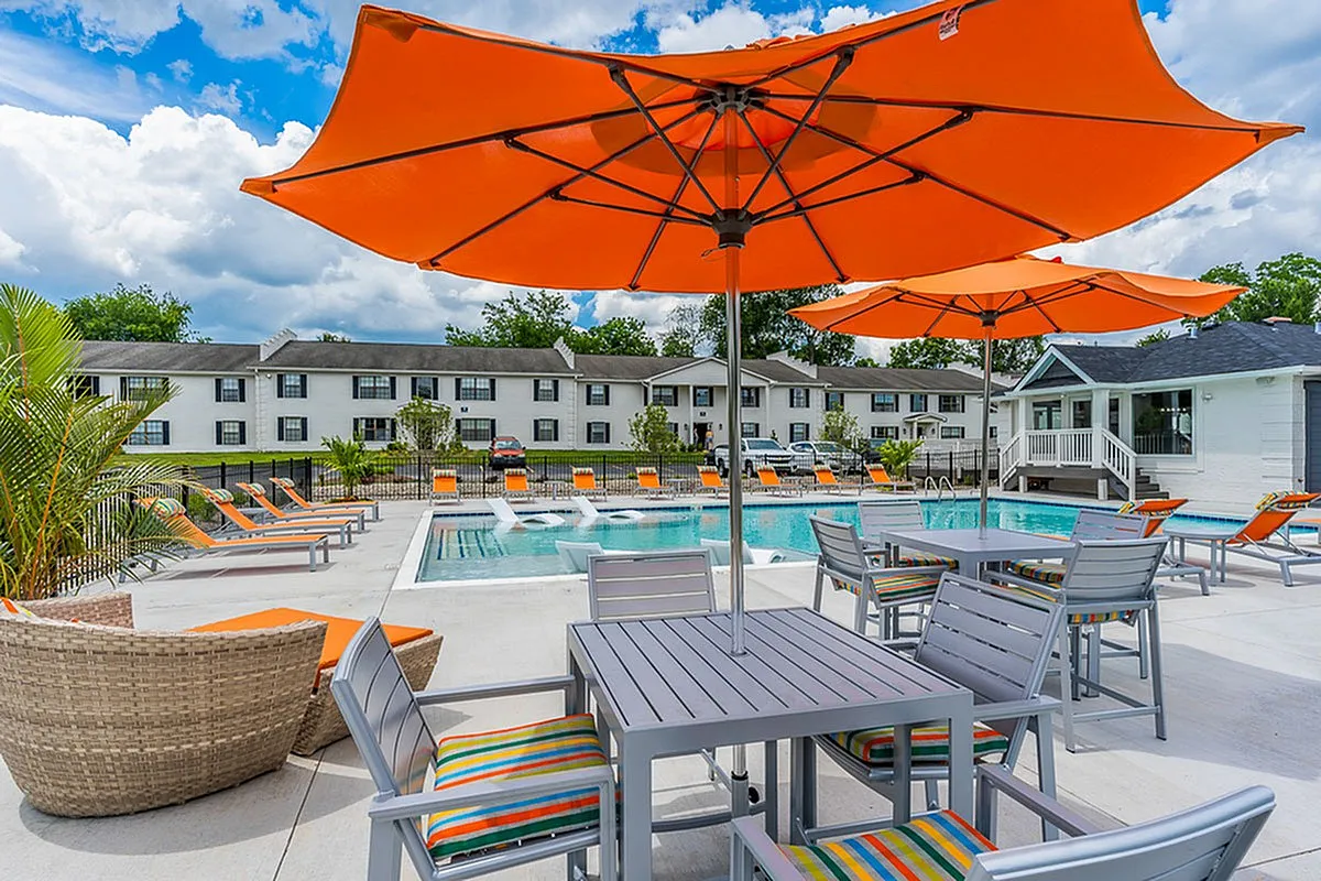 Inviting outdoor pool area at The Colony at the Oaks Apartments with vibrant orange umbrellas, stylish lounge chairs, and lush greenery, perfect for relaxation and entertaining.