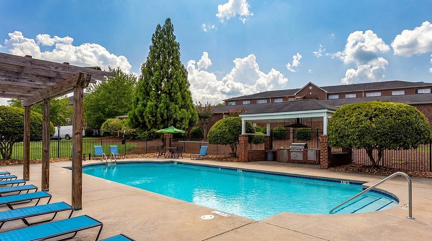 Inviting outdoor pool with lounge chairs under clear skies, set against lush greenery and a stylish brick building at Morgan Ridge Apartment in Winston-Salem