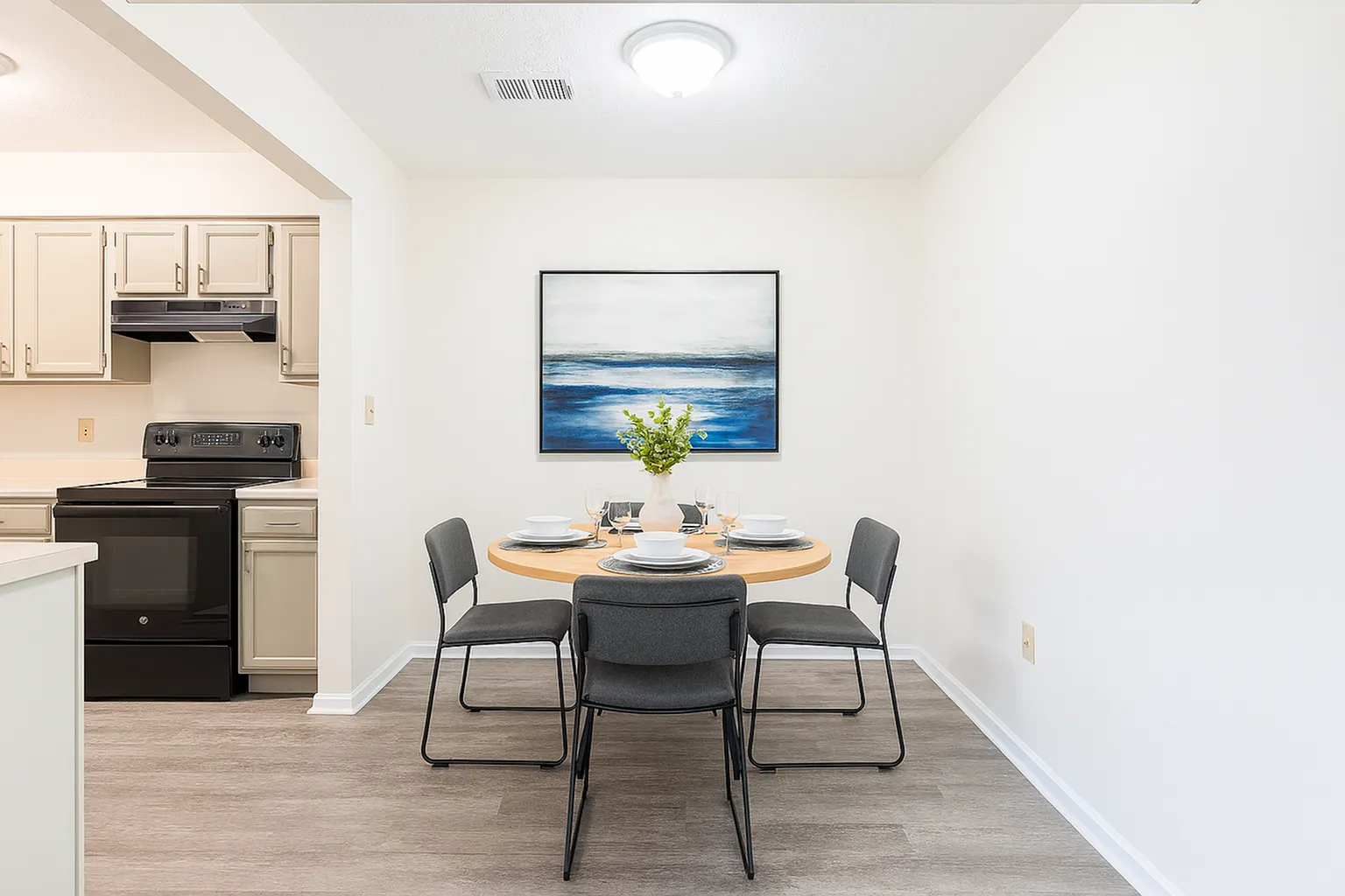 Elegant dining area showcasing a round table set for four, adjacent to a modern kitchen with sleek cabinetry and stylish flooring. Minimalist decor enhances the serene ambiance.