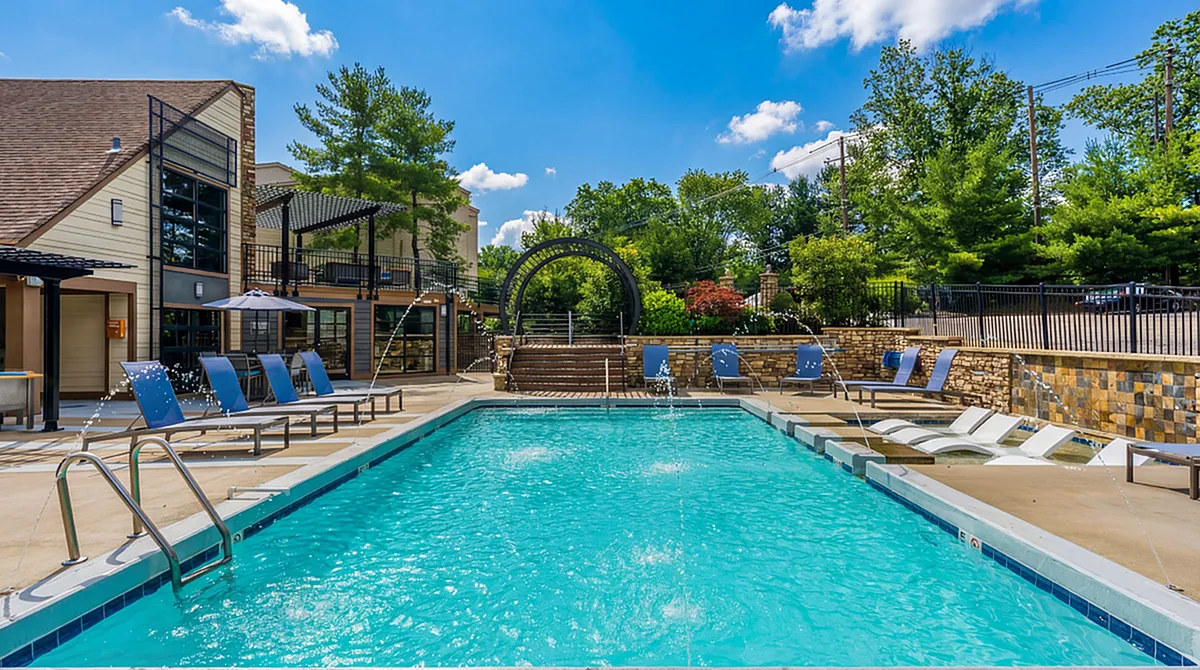 Luxurious outdoor pool area featuring modern lounge chairs, vibrant fountains, and lush greenery under a clear blue sky at Creeks at Kirklevington Apartments in Lexington KY