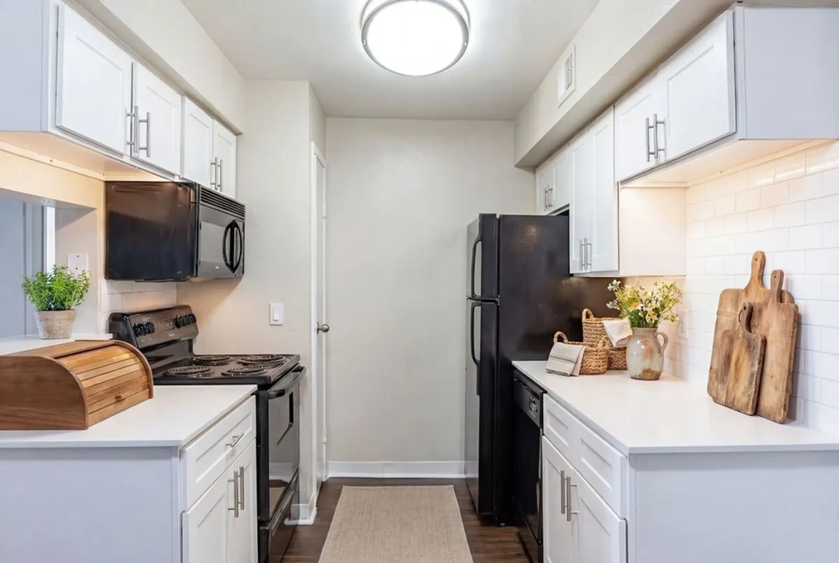 Modern kitchen with sleek white cabinets, black appliances, and stylish decor, creating a warm and inviting ambiance at Steepleway Downs Apartments in Houston