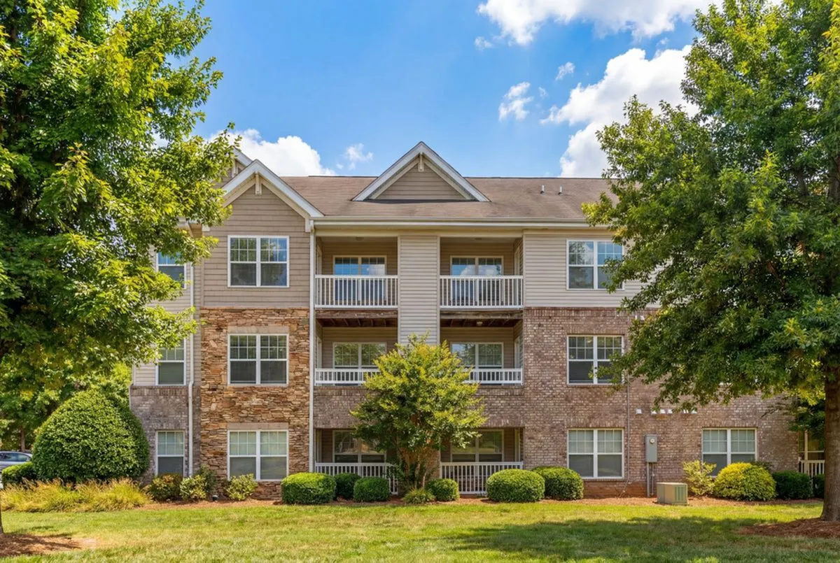 Charming apartment building with stone and brick facade, surrounded by lush greenery and vibrant trees at Stratford at Hillcrest Apartments in Winston-Salem.
