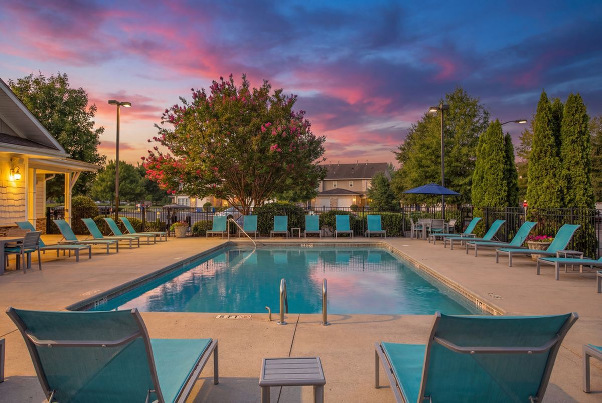 Inviting apartment complex pool area with vibrant lounge chairs, surrounded by lush greenery and a breathtaking sunset sky at Stratford at Hillcrest Apartments at Dusk