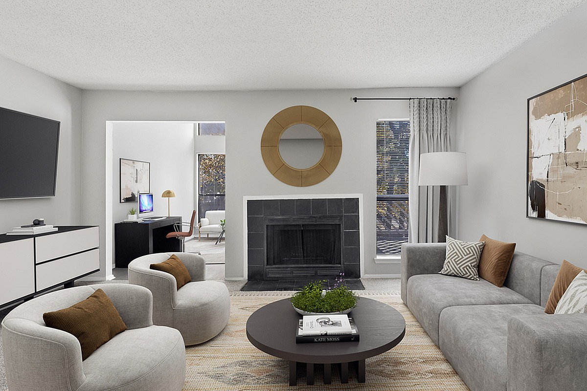 Modern living room at Park at Oak Ridge with stylish gray sofas, cozy armchairs, and a sleek fireplace. Elegant decor includes a round mirror and contemporary artwork. Abundant natural light from large windows enhances the inviting ambiance.