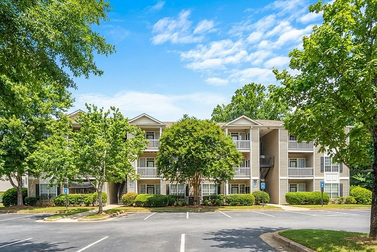 Charming apartment complex with balconies, surrounded by lush greenery and ample parking, under a clear blue sky at Lake St James in Conyers, GA.