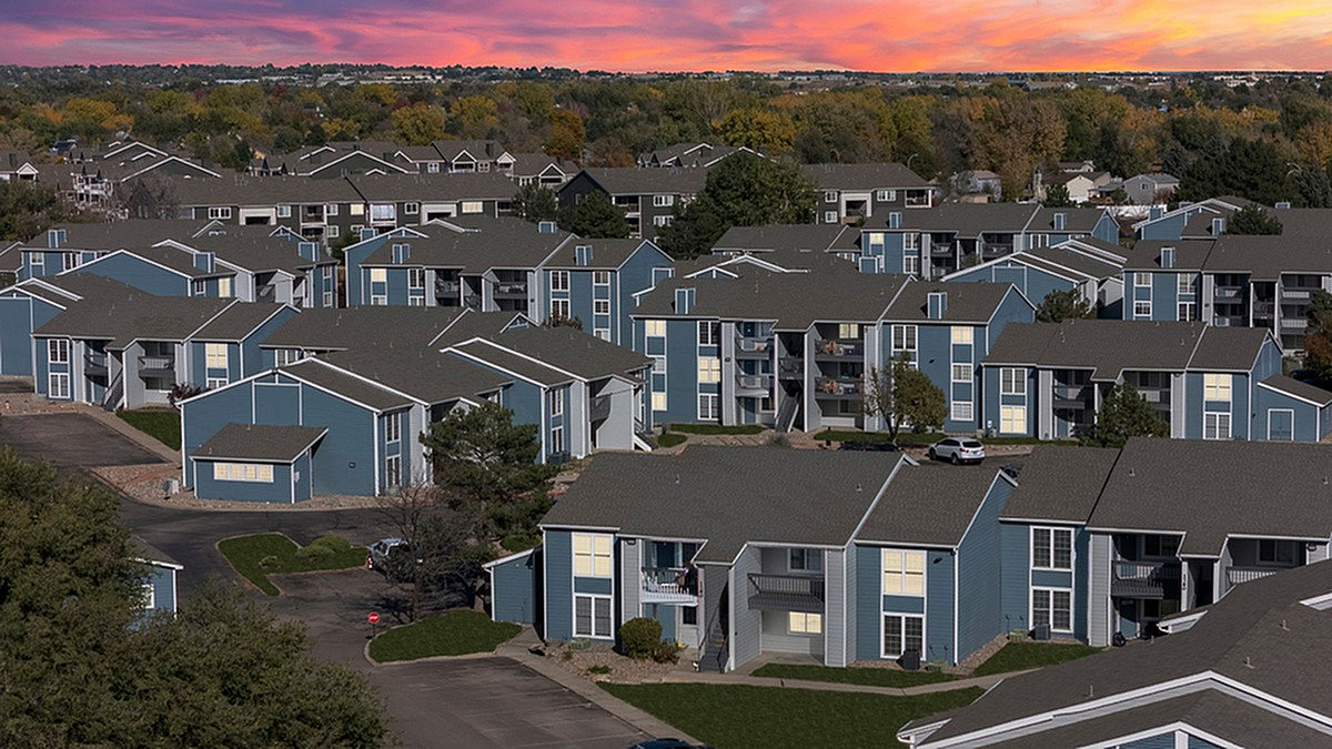 Charming apartment community in Colorado Springs, Antero Apartments, featuring blue, multi-level buildings, surrounded by lush greenery and a vibrant sunset sky.