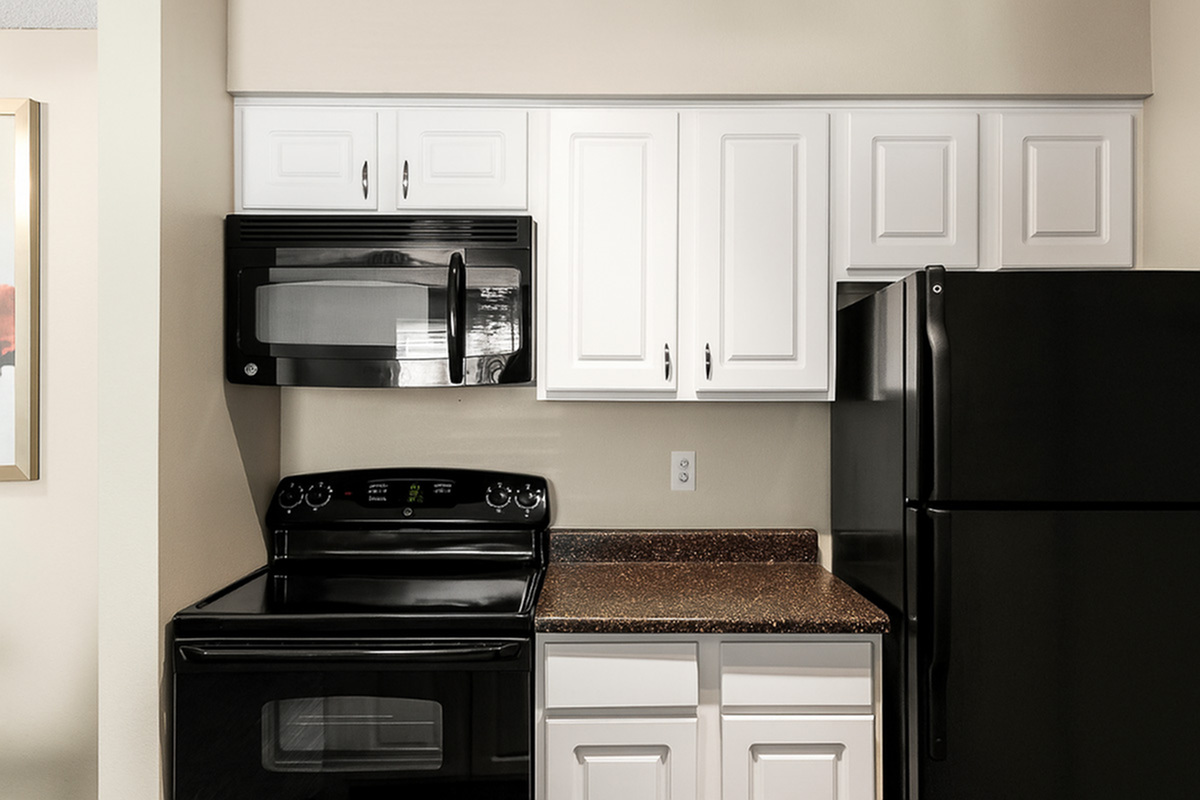 Modern kitchen at Antero Apartments with sleek black appliances, elegant white cabinetry, and a polished granite countertop.