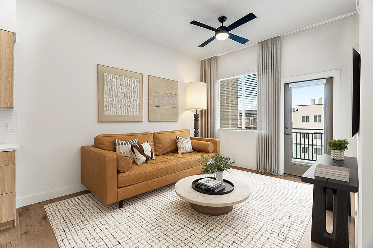 Chic modern living room featuring a stylish tan leather sofa, elegant artwork, and natural light pouring through wide windows onto a plush textured rug.