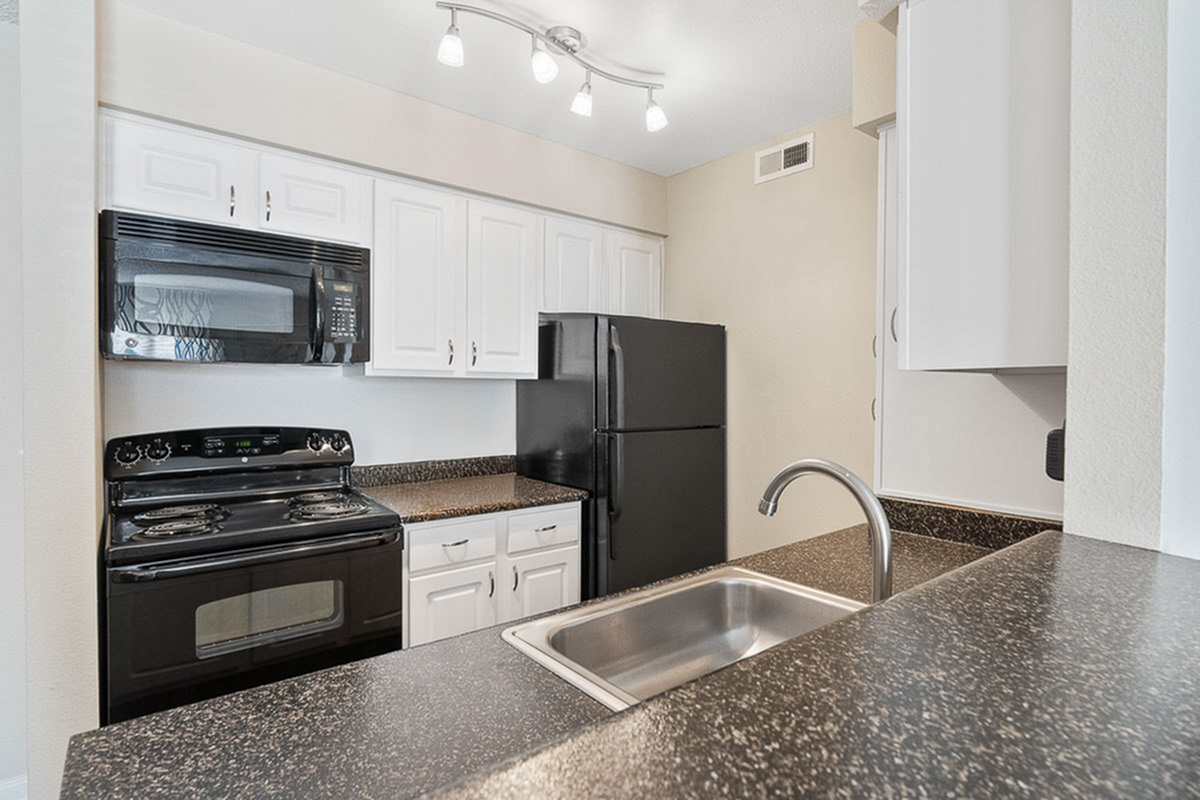 Modern kitchen at Antero Apartments with sleek black appliances, elegant white cabinetry, and stylish lighting.