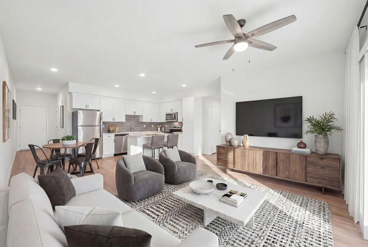 Chic open-plan living area with a modern kitchen, stylish furnishings, and a large wall-mounted TV, exuding comfort and elegance at Summit on Boulder Apartments near Las Vegas
