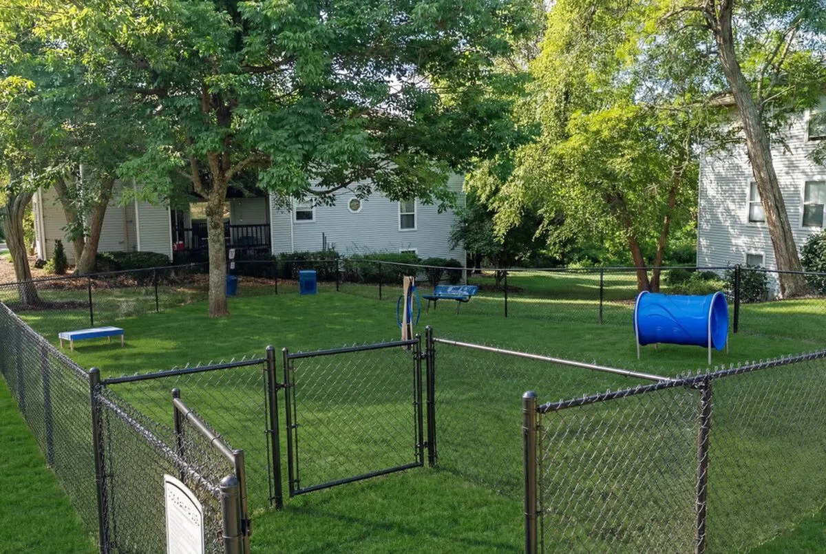 Inviting fenced dog park with agility equipment, lush grass, and shaded areas, perfect for pet-friendly living at Retreat at Stillmeadow Apartments