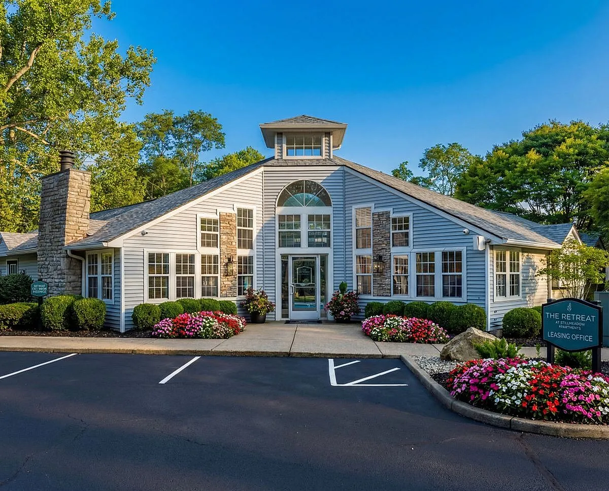 Charming community building at The Retreat, showcasing elegant architecture with large windows, vibrant flower beds, and lush green surroundings under a clear blue sky at Retreat at Stillmeadow Apartments in Columbus.