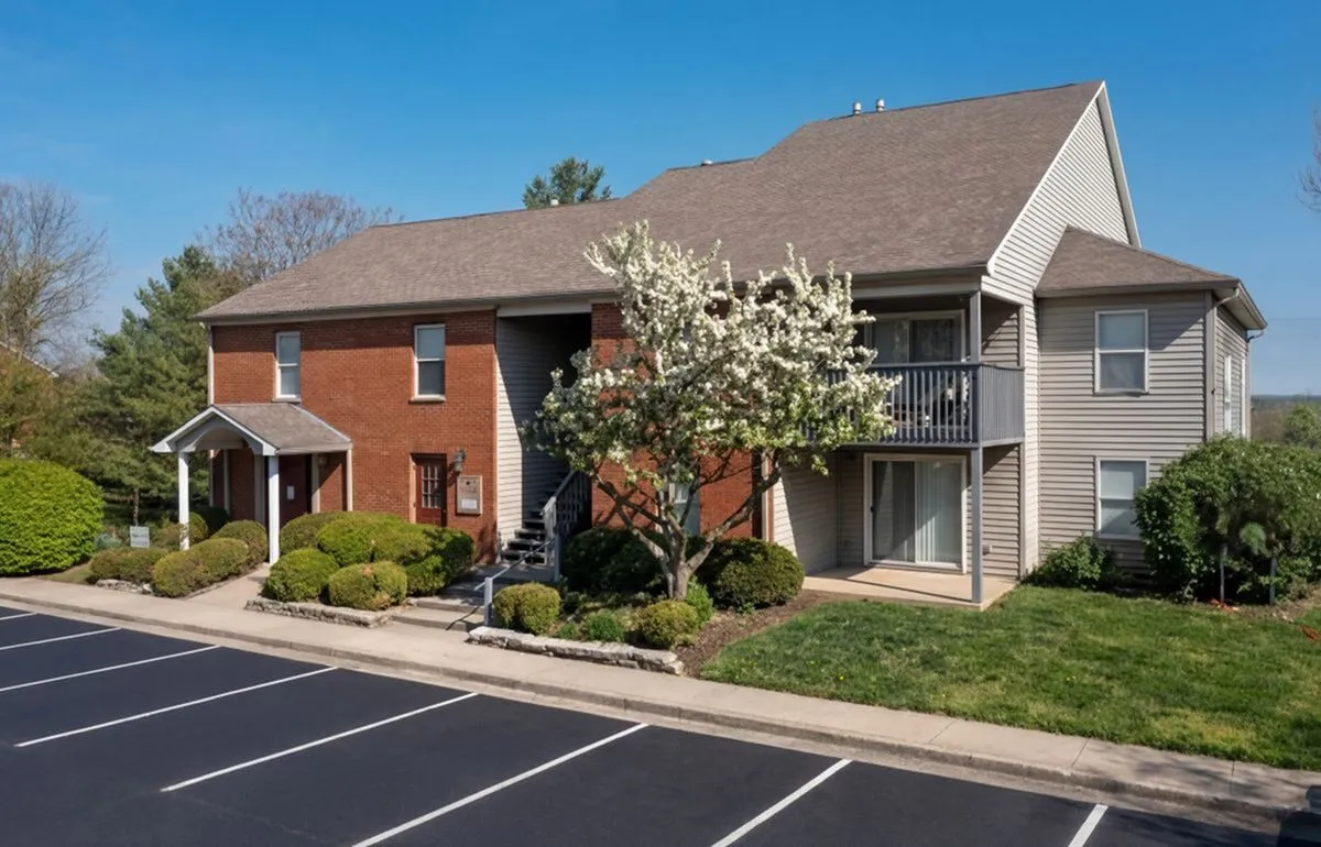 Charming apartment building with a mix of brick and siding, surrounded by lush greenery and blooming trees, offering spacious balconies for outdoor relaxation at Crown Pointe Apartments