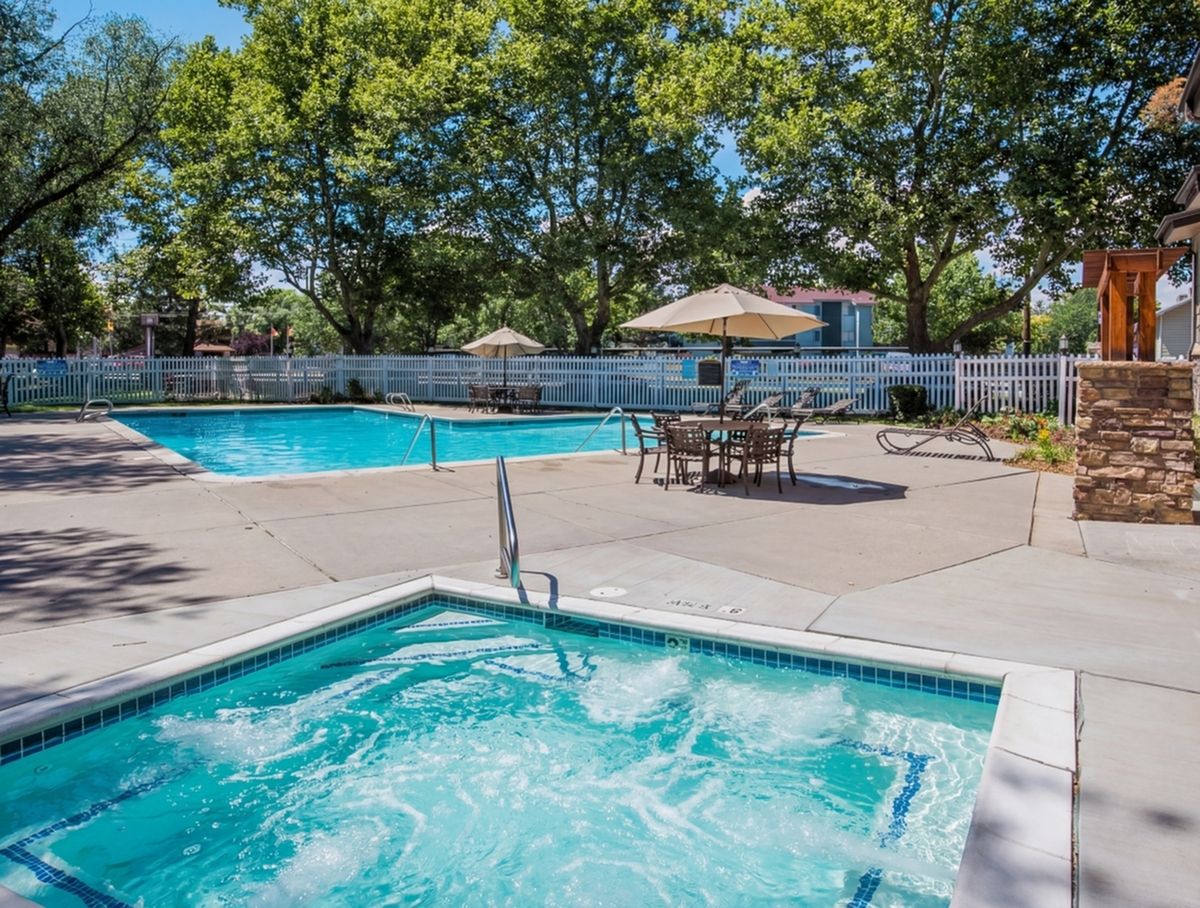 Inviting outdoor pool area featuring a bubbling hot tub and stylish patio seating under large umbrellas, surrounded by lush greenery.