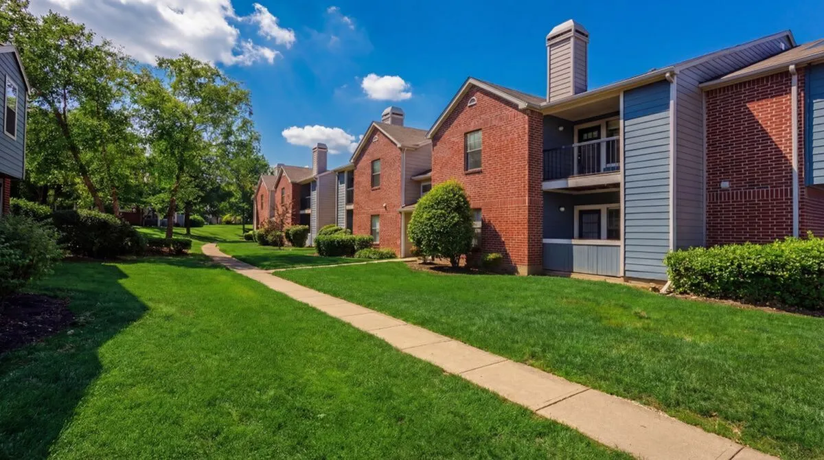 Charming brick apartment complex with lush green lawns and mature trees, perfect for serene living.