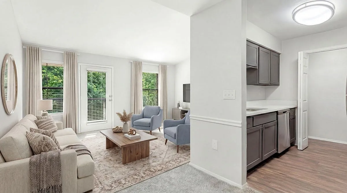 Elegant living room with cozy beige sofa, stylish blue armchairs, and a sleek modern kitchen with stainless steel appliances at Timber Hollow Apartments