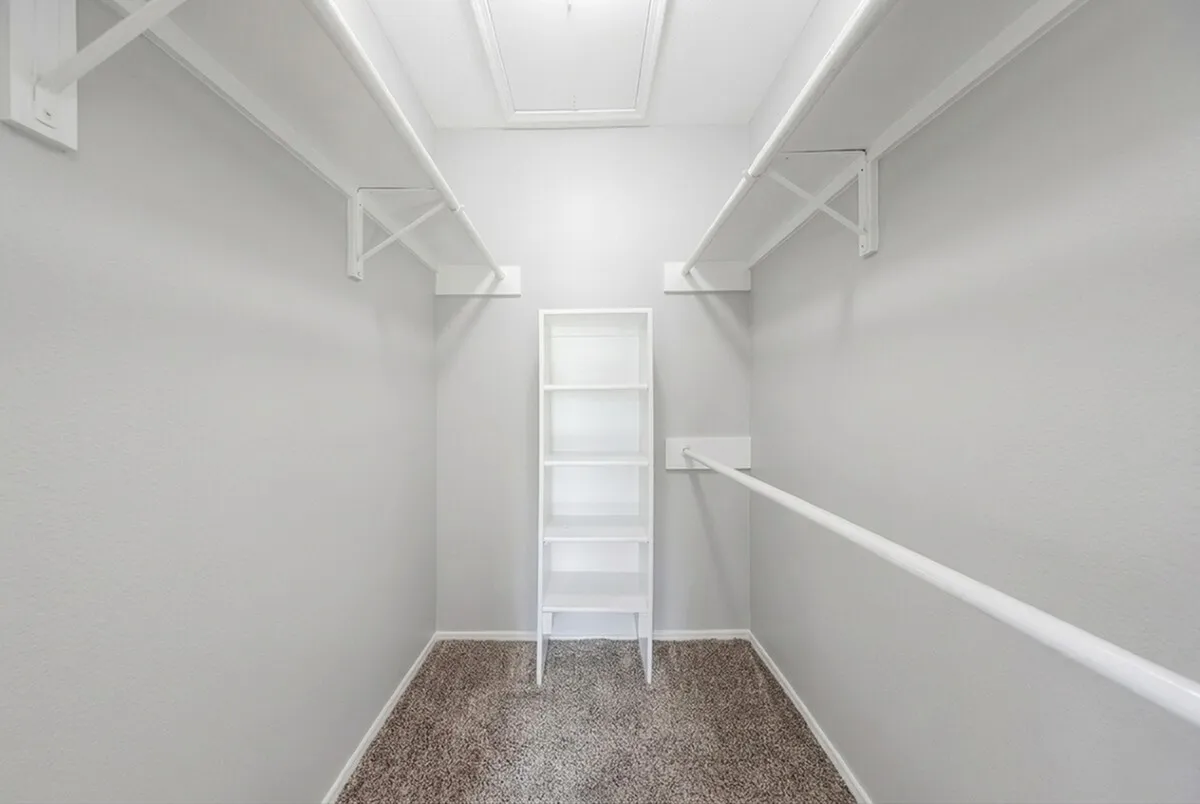 Bright, spacious walk-in closet at Timber Hollow Apartments with elegant shelving and ample hanging space, featuring neutral tones and plush carpeting.