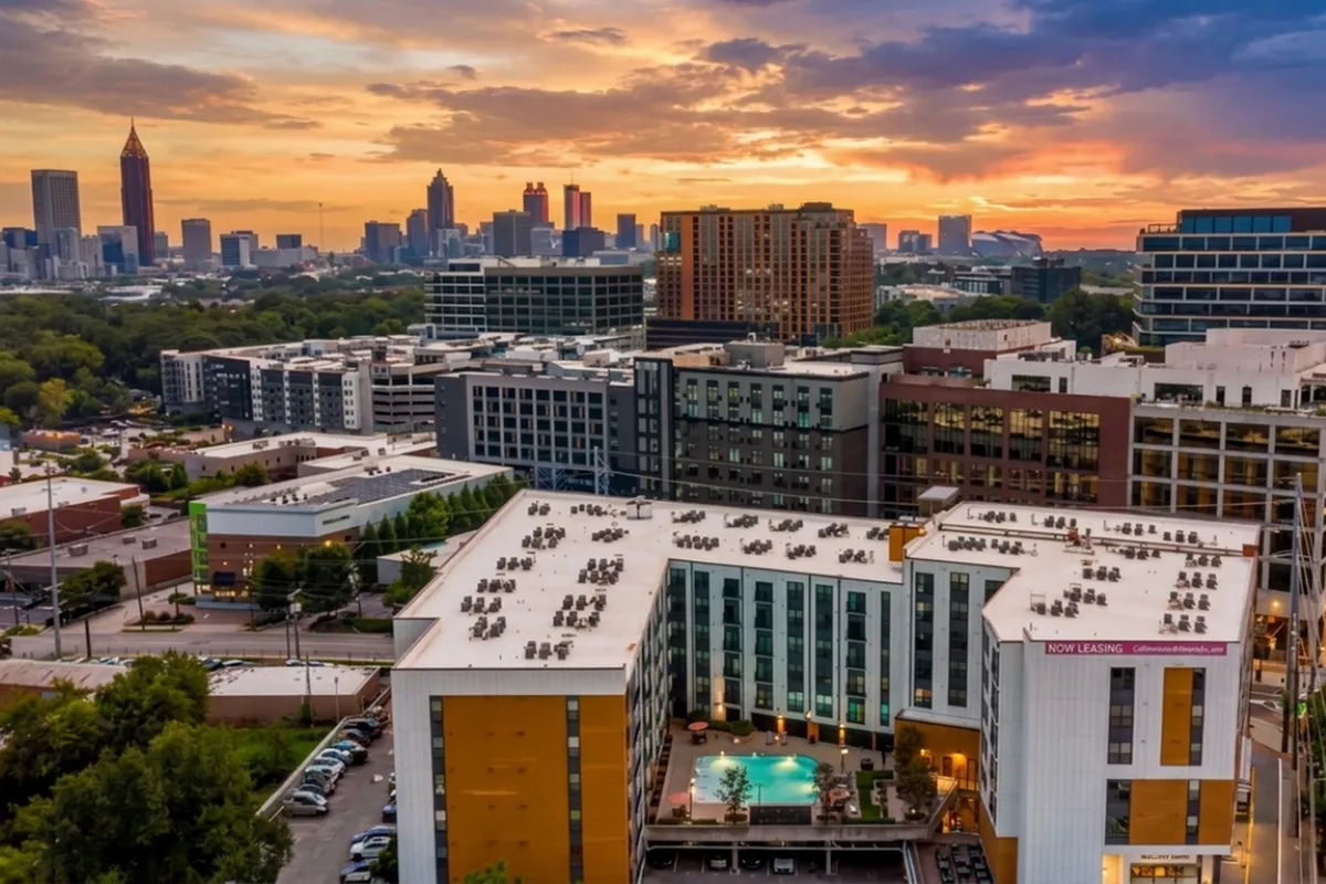 Stunning rooftop view of a modern apartment complex with a central pool, set against a vibrant city skyline at sunset.