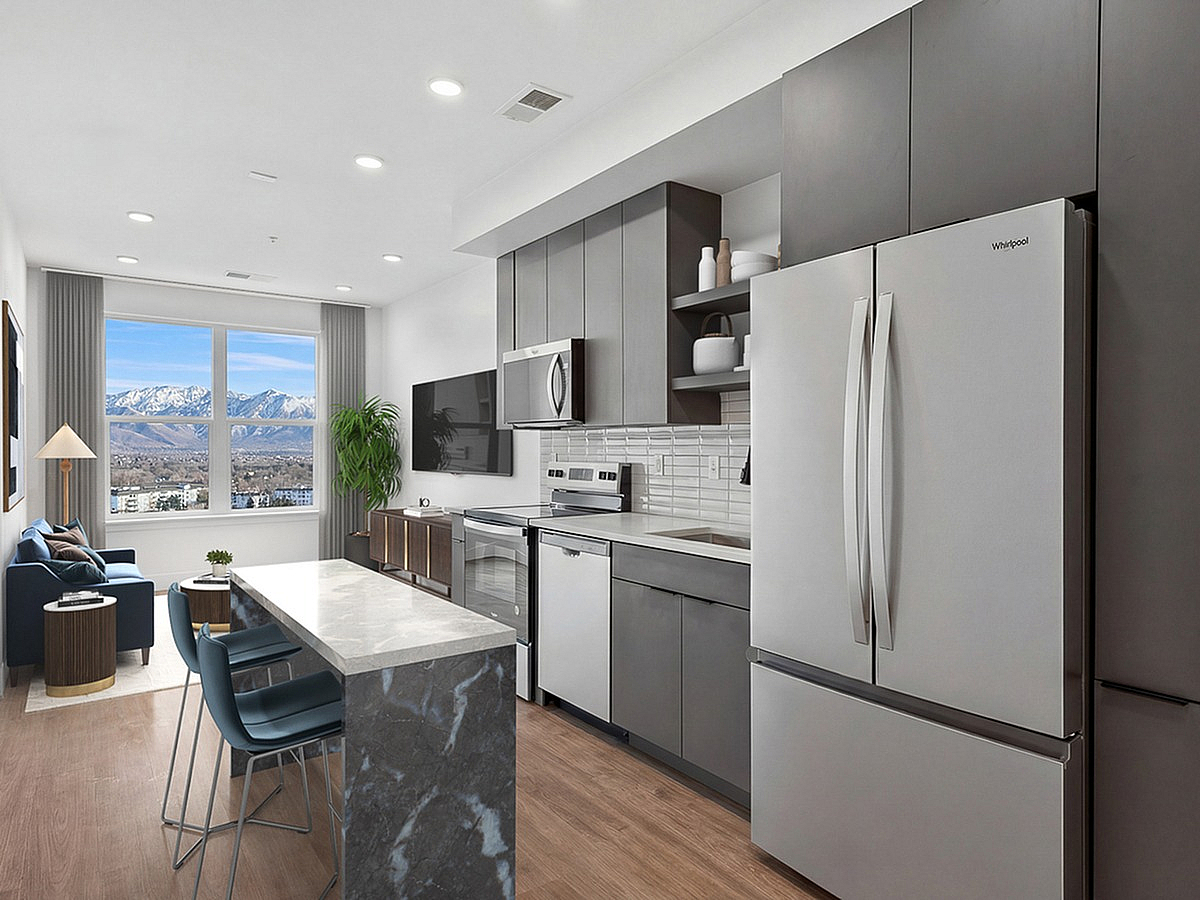Elegant modern kitchen featuring sleek appliances and a stylish breakfast bar, opening to a bright living area with panoramic mountain views at The Westerly Apartments in Millcreek.