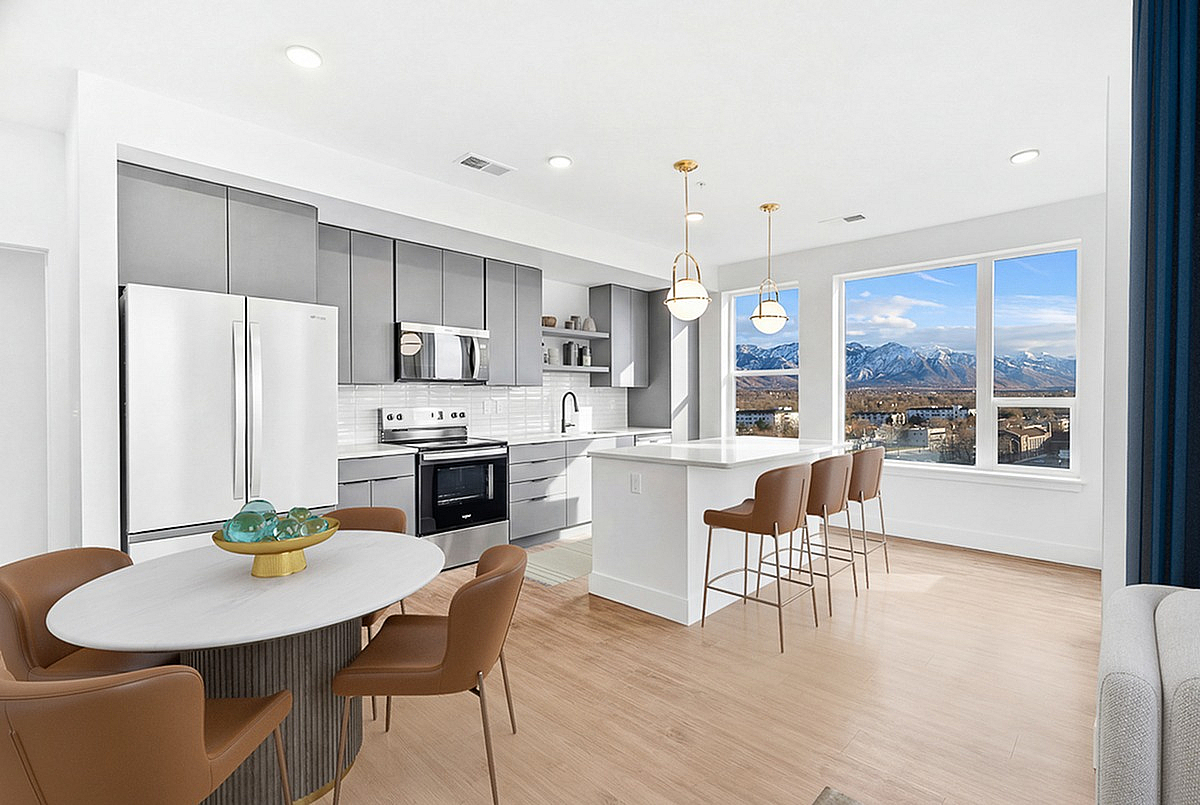 Modern open-concept kitchen and dining area with sleek gray cabinetry, elegant pendant lighting, and stunning mountain views through large windows at The Westerly Apartments in Millcreek, UT.