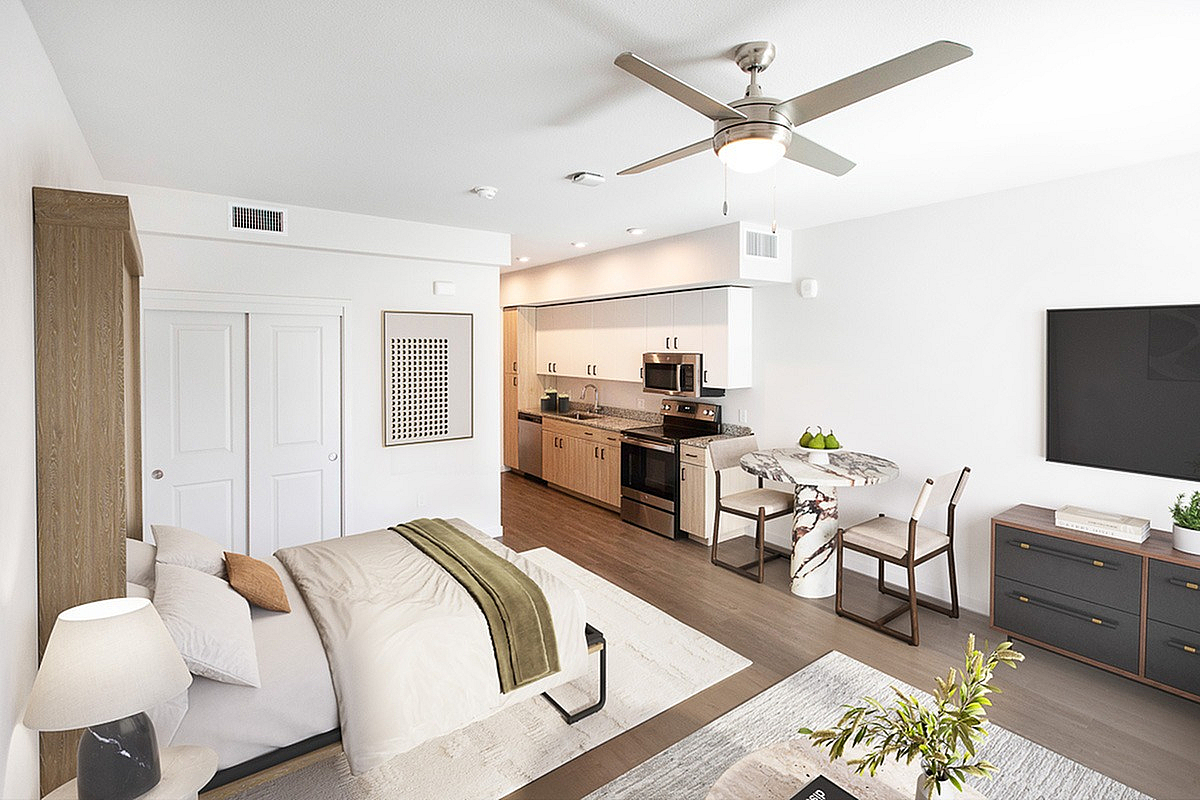 Modern studio apartment featuring a cozy bed area, sleek kitchen with stainless steel appliances, and a chic dining space under a stylish ceiling fan.