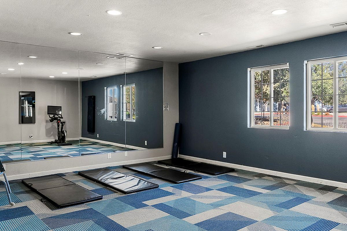 Modern fitness studio with stylish blue checkered flooring, large mirrors, and natural light through two windows, featuring exercise equipment and mats for versatile workouts.