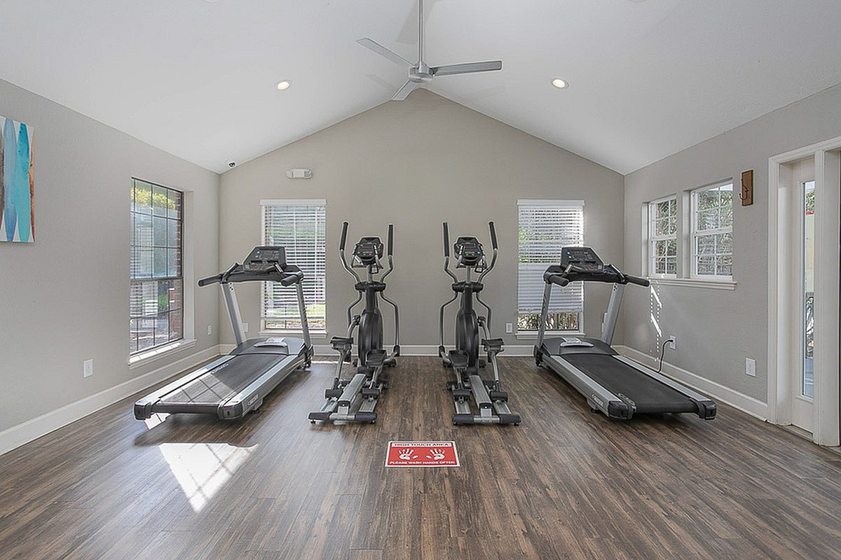 Modern fitness room at Autumn Ridge Apartments with large windows, featuring treadmills and elliptical machines, perfect for a revitalizing workout experience.