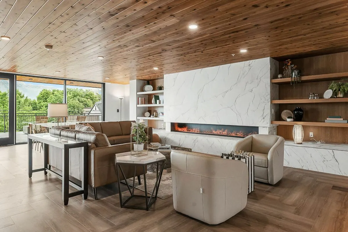 Modern clubroom with elegant decor, featuring a large flat-screen TV, cozy seating, and a sleek fireplace. Bright natural light pours in through expansive windows showcasing a lush green view  at Current Apartments in Murray Utah