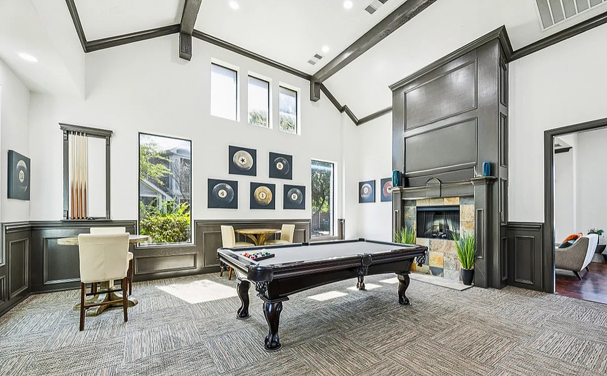 Luxurious game room featuring a sleek pool table, elegant seating area, and a cozy fireplace under high ceilings at Enclave on Golden Triangle Apartments in Fort Worth Texas