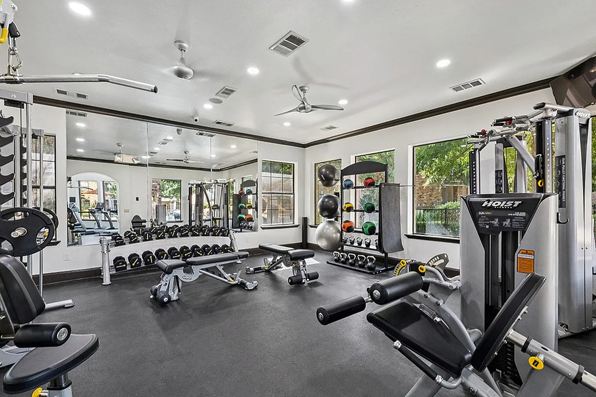 Modern fitness center with advanced gym equipment, free weights, and natural light streaming through large windows at Enclave on Golden Triangle Apartments in Fort Worth Texas