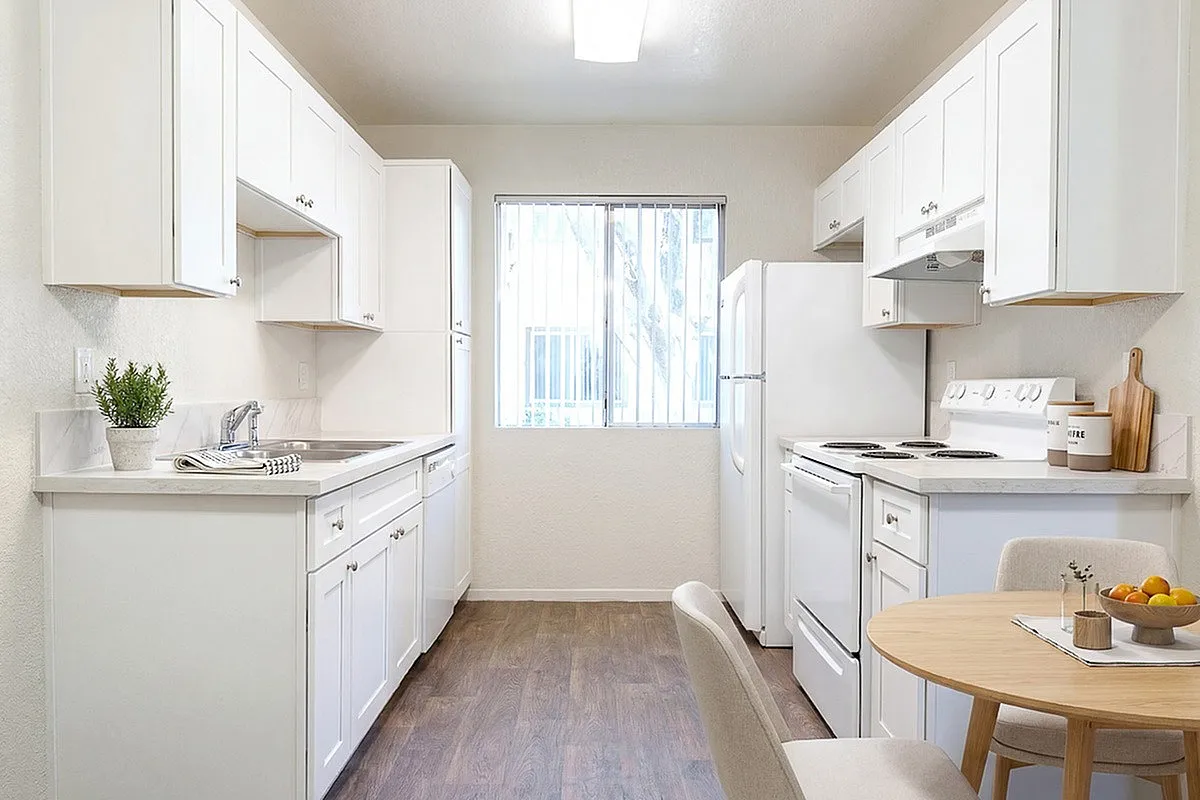 Bright and inviting kitchen at Camelot Apartments with modern white cabinets, sleek countertops, and warm wood flooring, perfect for culinary adventures.