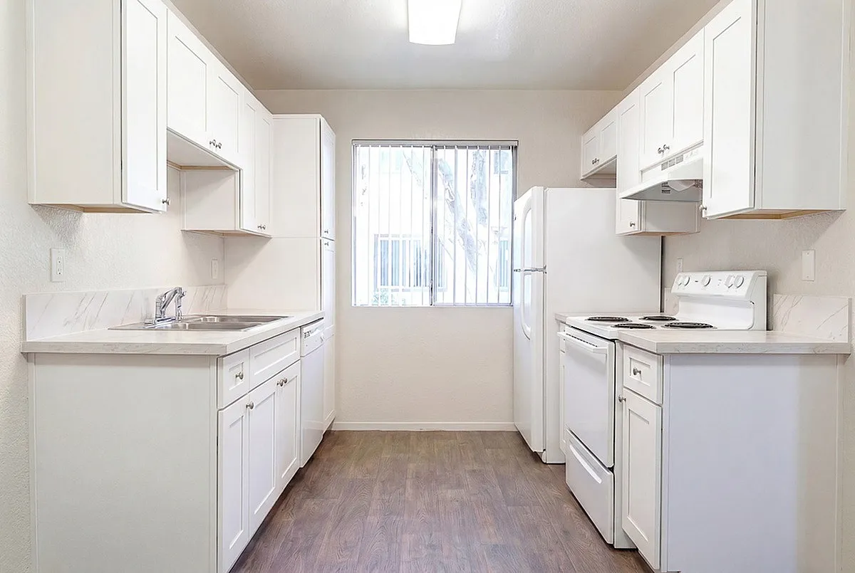 Bright modern kitchen at Camelot Apartments with white cabinetry, sleek countertops, and natural light through a large window.