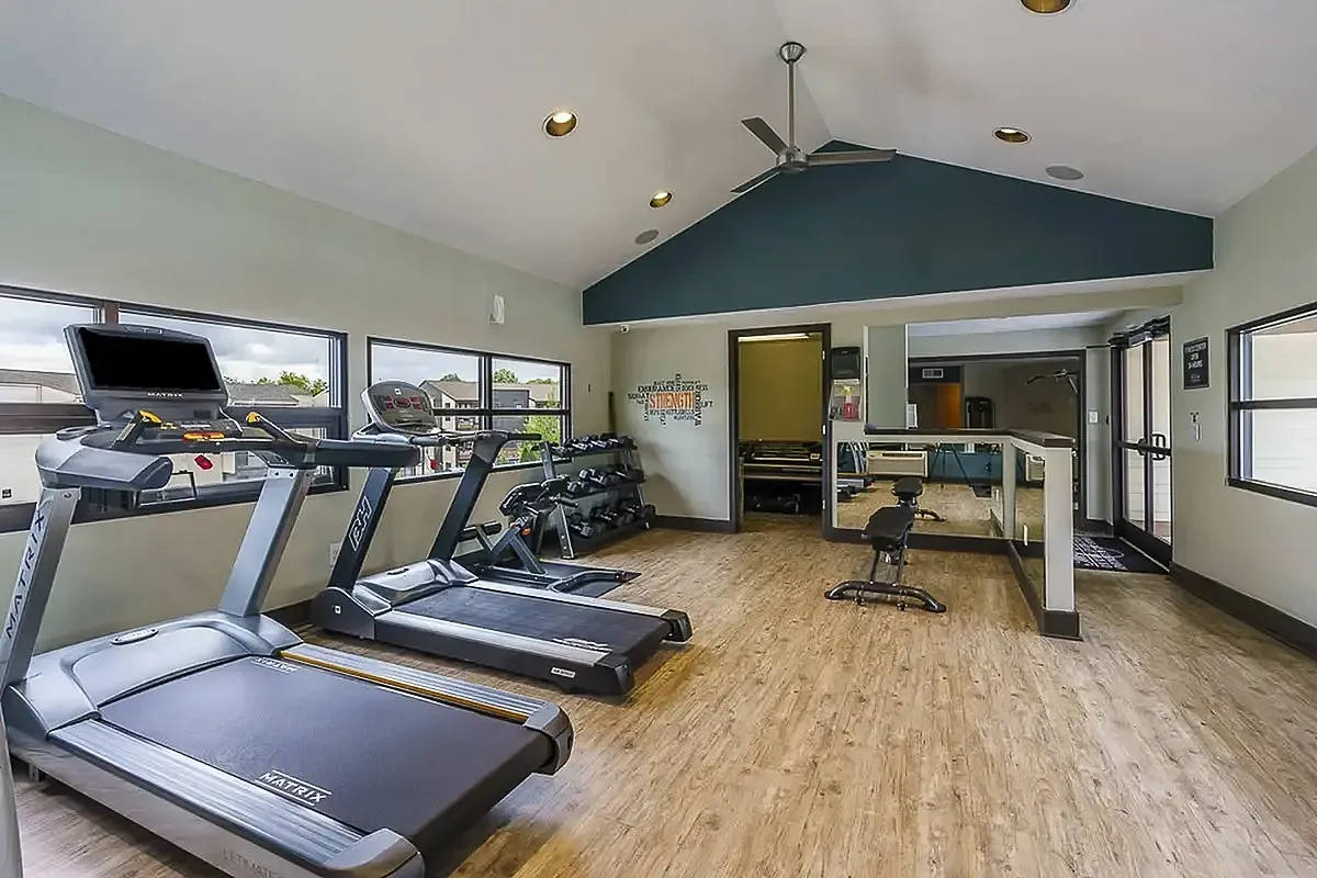 Bright and modern fitness center with state-of-the-art equipment, sleek wooden floors, and abundant natural light at The Creeks on Kirklevington Apartments.
