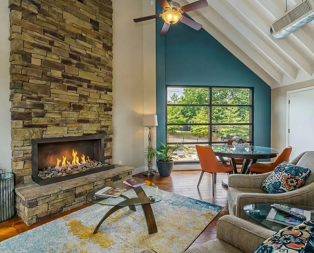 Inviting clubroom featuring a modern stone fireplace, vaulted ceiling, and large windows offering a scenic view, complemented by stylish furniture and vibrant decor at Creeks at Kirklevington Apartments in Lexington, KY.