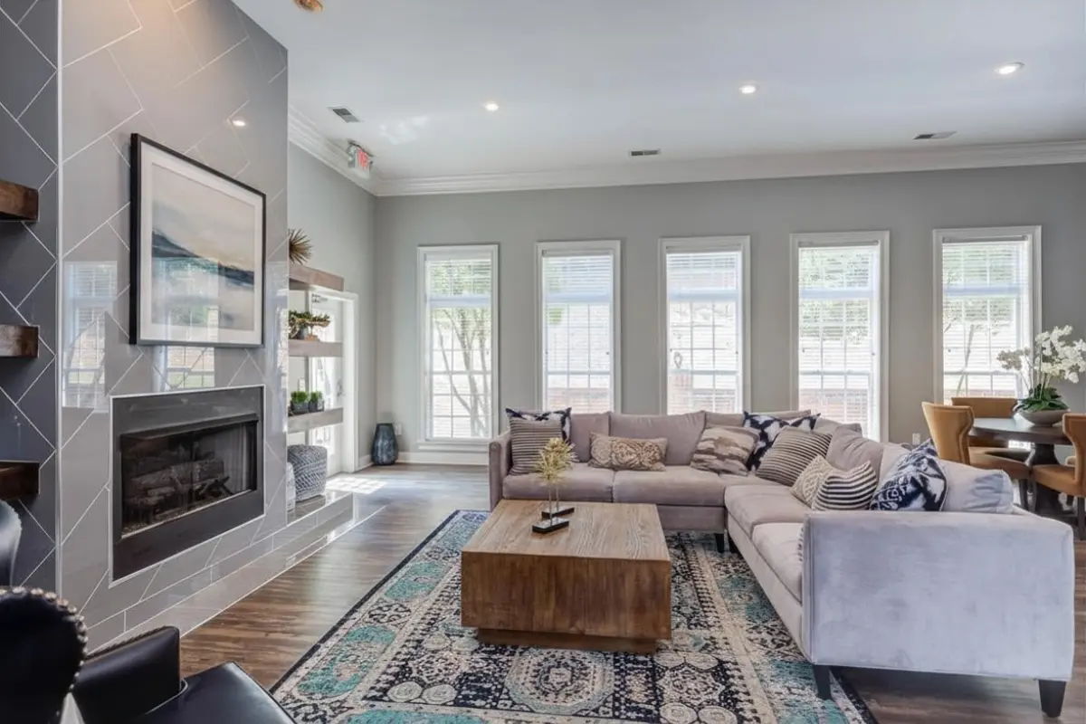 Elegant clubroom at Morgan Ridge Apartments with a cozy L-shaped sofa, chic coffee table, and vibrant rug, featuring a modern fireplace and large windows for ample natural light.