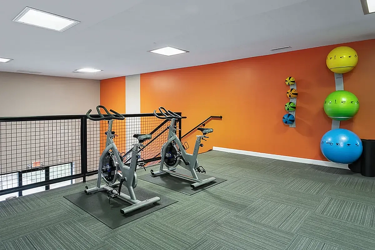 Modern gym area with vibrant orange walls featuring exercise bikes and colorful fitness balls for an energizing workout experience at Park at Oak Ridge Apartments.